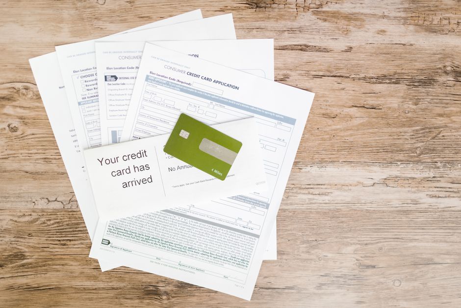 A collection of white papers with printed text and blank fields, fanned out on a light wooden surface, accompanied by a green credit card placed on top. The papers include a prominent message indicati